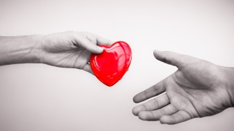 one hand gives a red heart to another hand